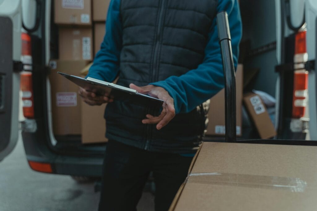 Courier uses clipboard to manage parcel delivery from van load.