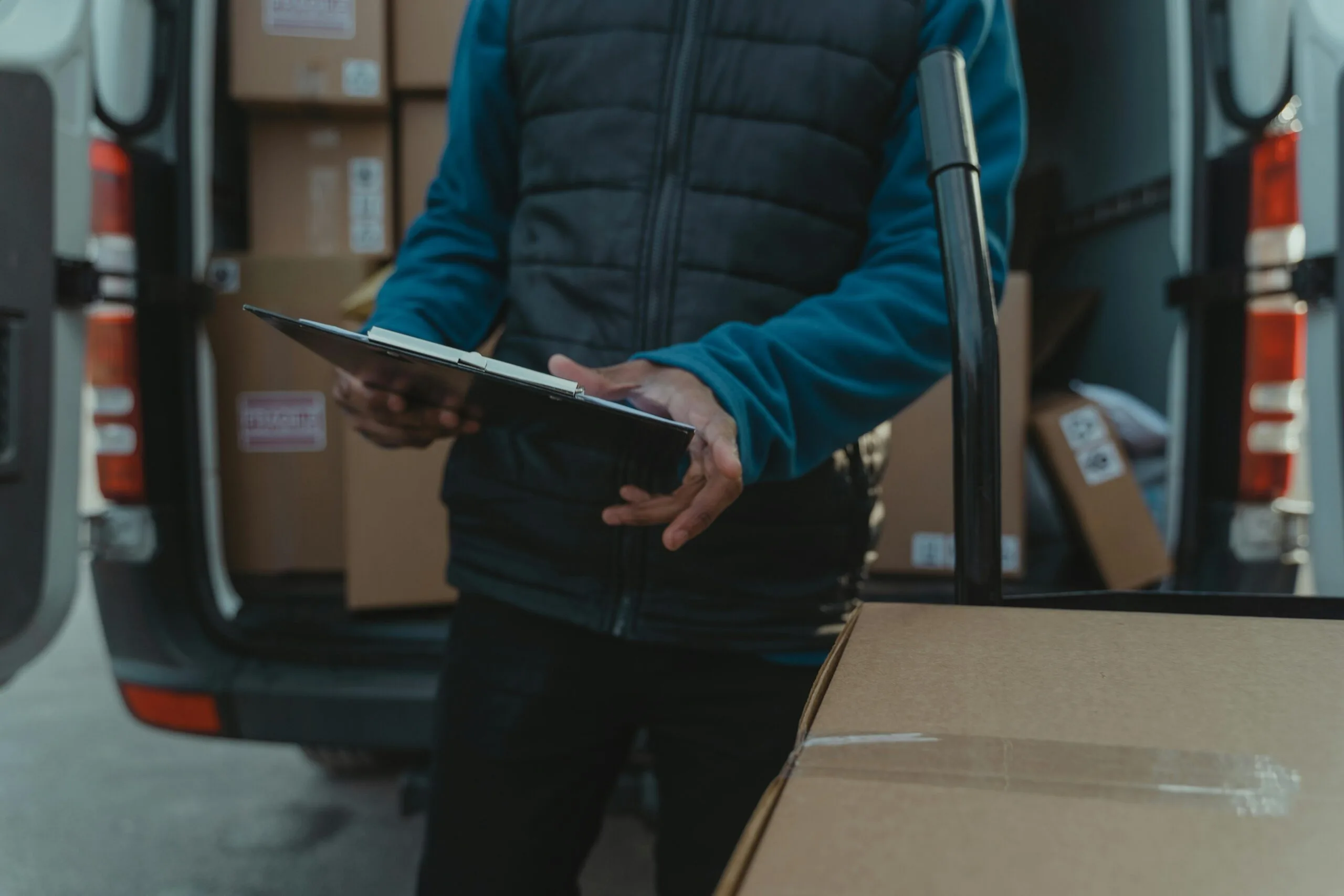 Courier uses clipboard to manage parcel delivery from van load.
